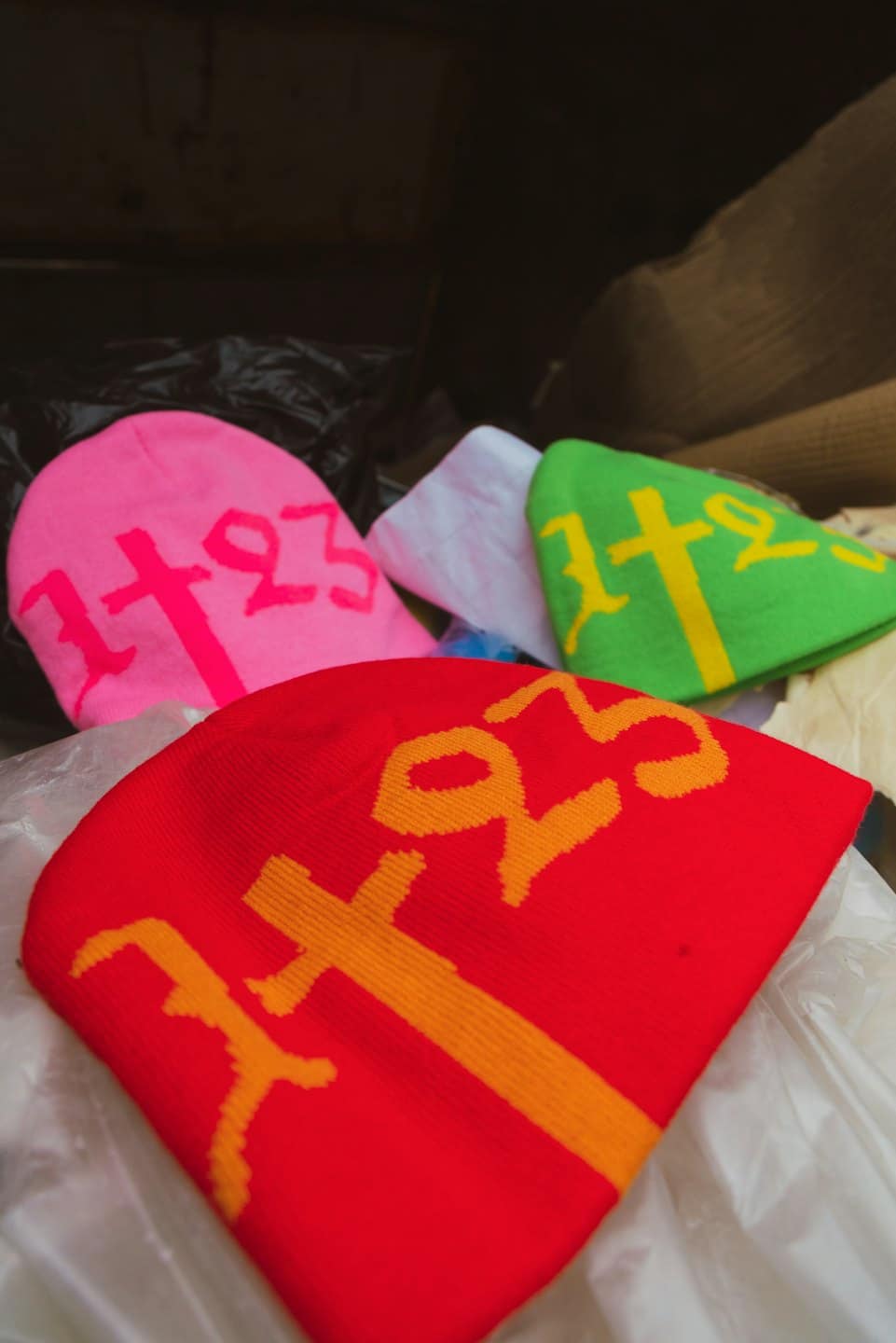 Kolorowe czapki beanie z napisem 1+23 w pudełku.