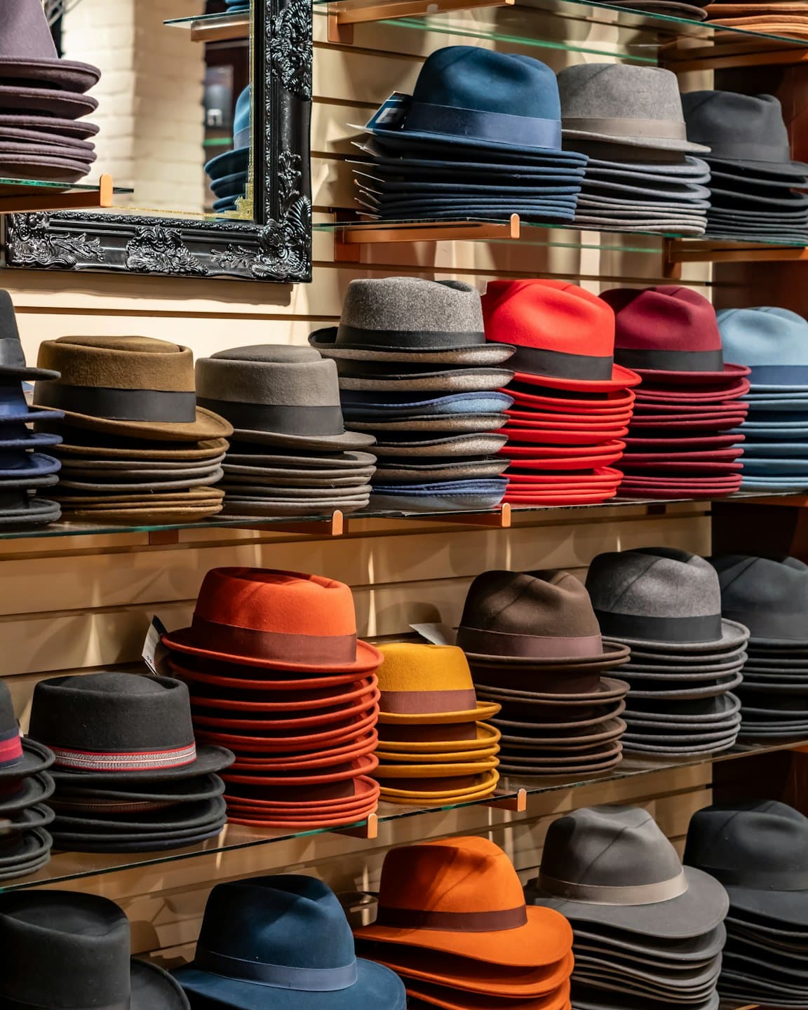 Filcowe kapelusze fedora w różnych kolorach ułożone na szklanych półkach.